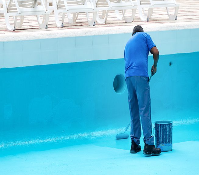 Unrecognizable worker repainting swimming pool in blue colour. Reconstruction process