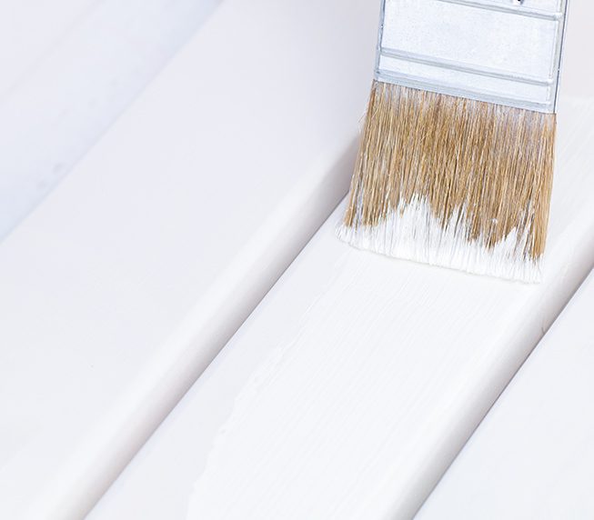 Brush with white paint is on boards. Painting of new wood chair.