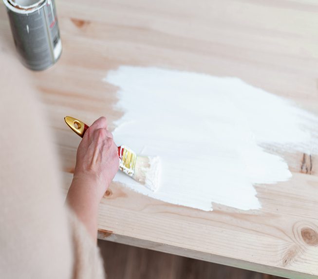 Female hand with a brush to apply white paint on wooden furniture. The concept of renovation, the furniture update.